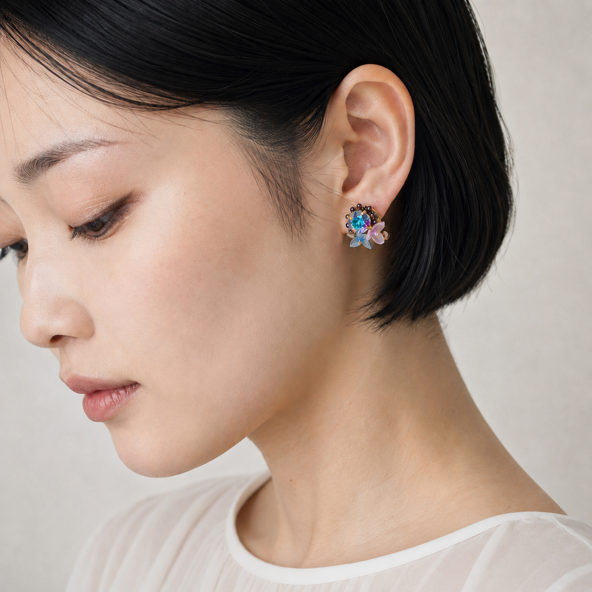 A close-up of a woman with short black hair wearing a colorful, flower-shaped stud earring with blue, pink, and purple details.