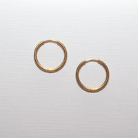A pair of thin gold hoop earrings on a light gray textured background.