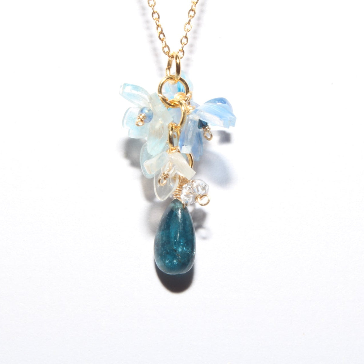 A gold chain necklace with a unique floral and teardrop pendant. The pendant features light blue and milky white flower-like beads at the top, a small clear crystal, and a dangling teardrop-shaped blue stone at the bottom.