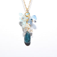 A gold chain necklace with a unique floral and teardrop pendant. The pendant features light blue and milky white flower-like beads at the top, a small clear crystal, and a dangling teardrop-shaped blue stone at the bottom.