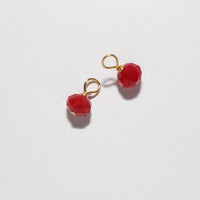 A pair of small drop earrings featuring faceted red beads suspended from gold-colored rings, displayed on a clean white background.