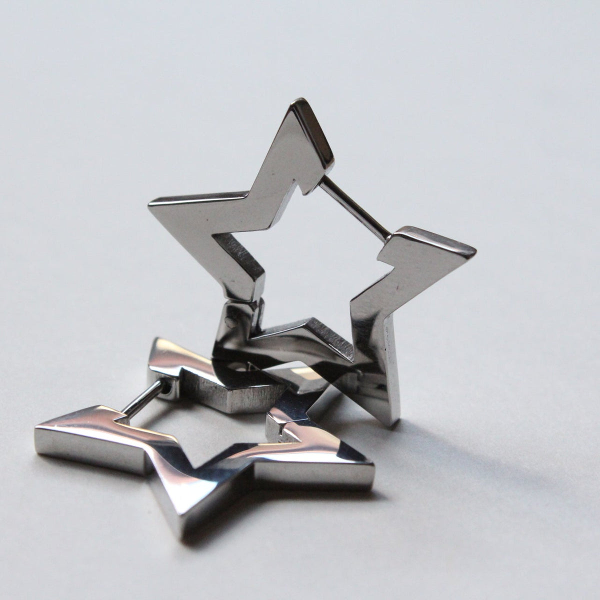 A pair of metallic silver star-shaped earrings with a geometric, faceted design, displayed on a light gray surface.