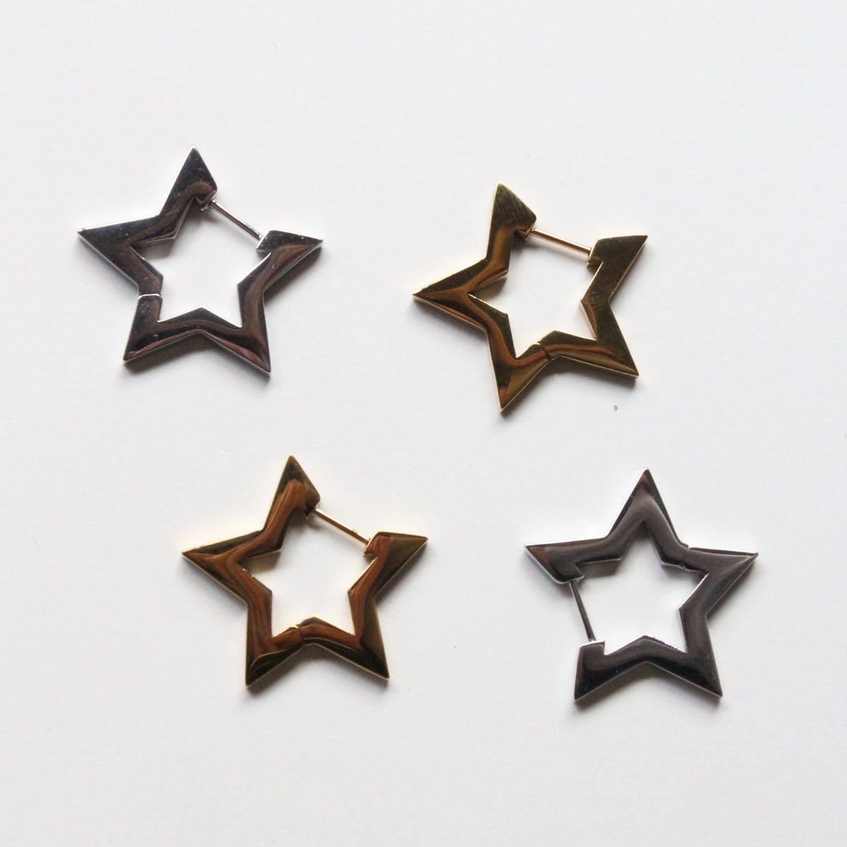 Four star-shaped hoop earrings in dark metallic finishes, arranged on a plain white background.