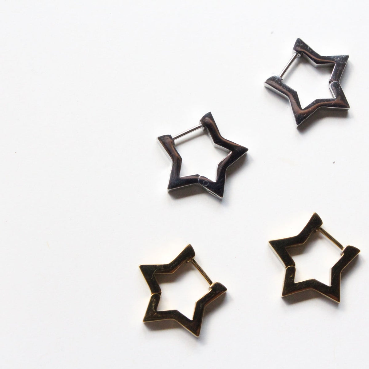 Four star-shaped hoop earrings with a dark metallic finish, arranged on a plain white background.
