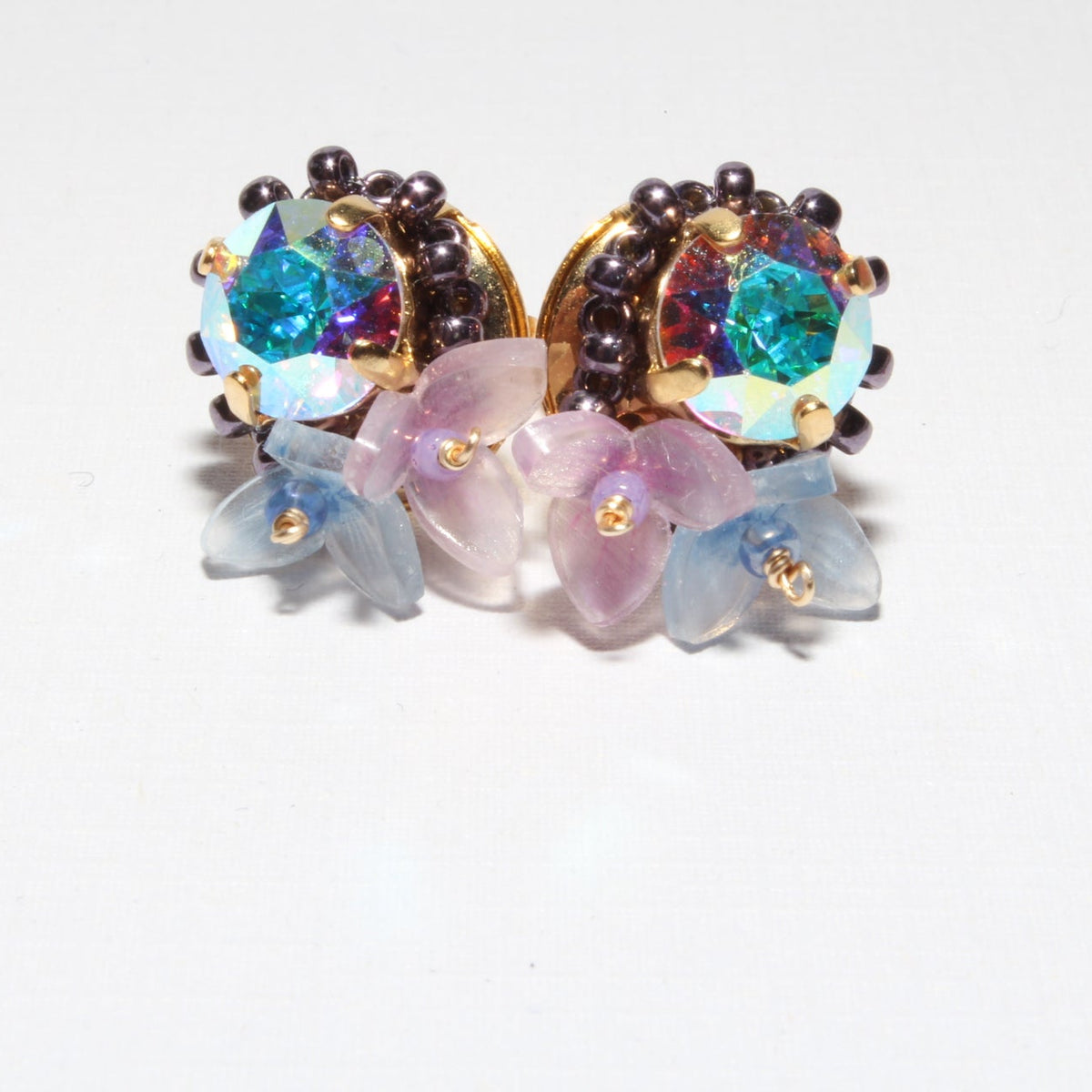A pair of vintage-style floral stud earrings with iridescent blue-green stones, dark brown bead accents, and translucent pink and blue flower petals on a white background.