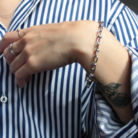 Person wearing a blue and white striped shirt with a handmade  bracelet and ring on a blurred background