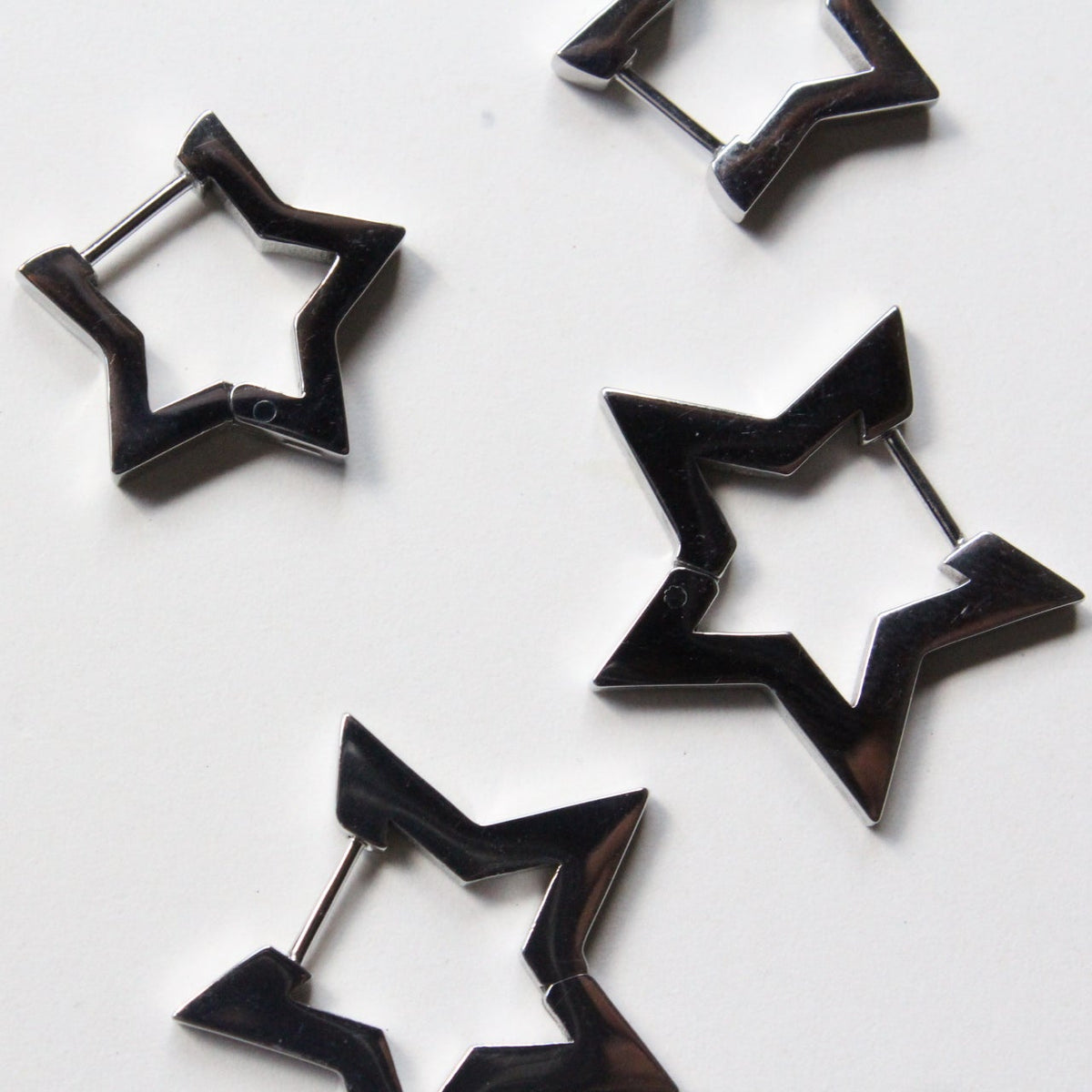 Four silver star-shaped hoop earrings with silver-toned posts, arranged on a plain white surface.