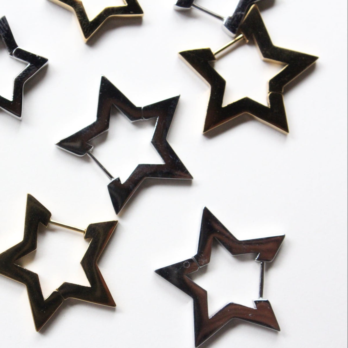 A set of star-shaped hoop earrings in a dark wood inlay with a gold-tone metal border, scattered on a plain white background.