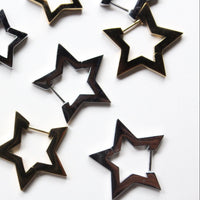 A set of star-shaped hoop earrings in a dark wood inlay with a gold-tone metal border, scattered on a plain white background.